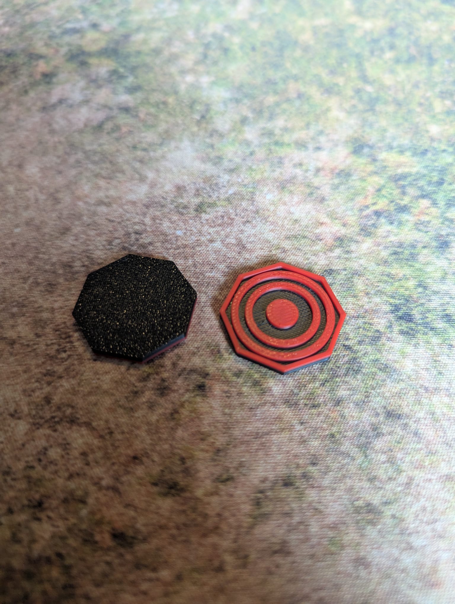 Two geometric shapes, one black octagon and one red and gray octagon, on a textured surface.